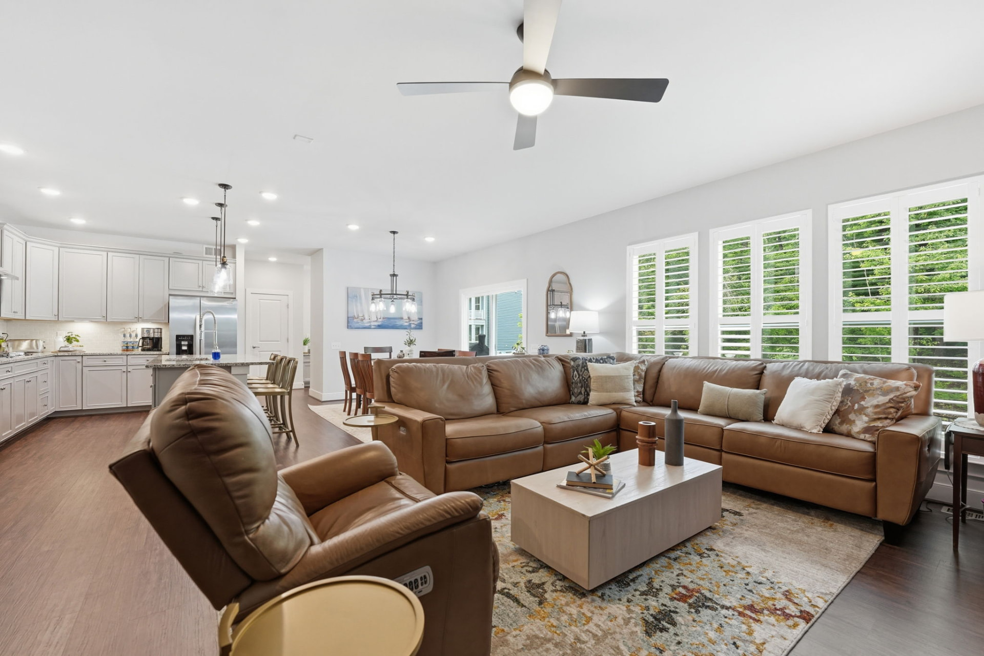 Open-plan model home great room staged with leather seating, dining area, and plantation shutters